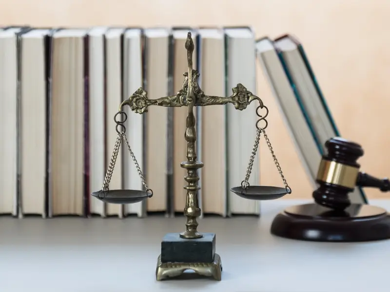 Eine Waage und ein Richterhammer stehen vor einer Bücherreihe