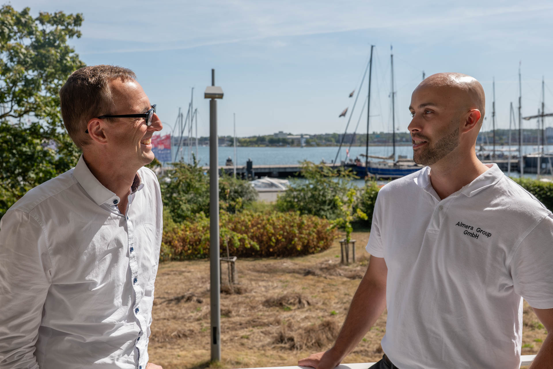 Digitalisierungsminister Dirk Schrödter und AImera Geschäftsführer Lino Griefer stehen sich gegenüber und sprechen miteinander. Im Hintergrund ist die Kieler Förde zu sehen.