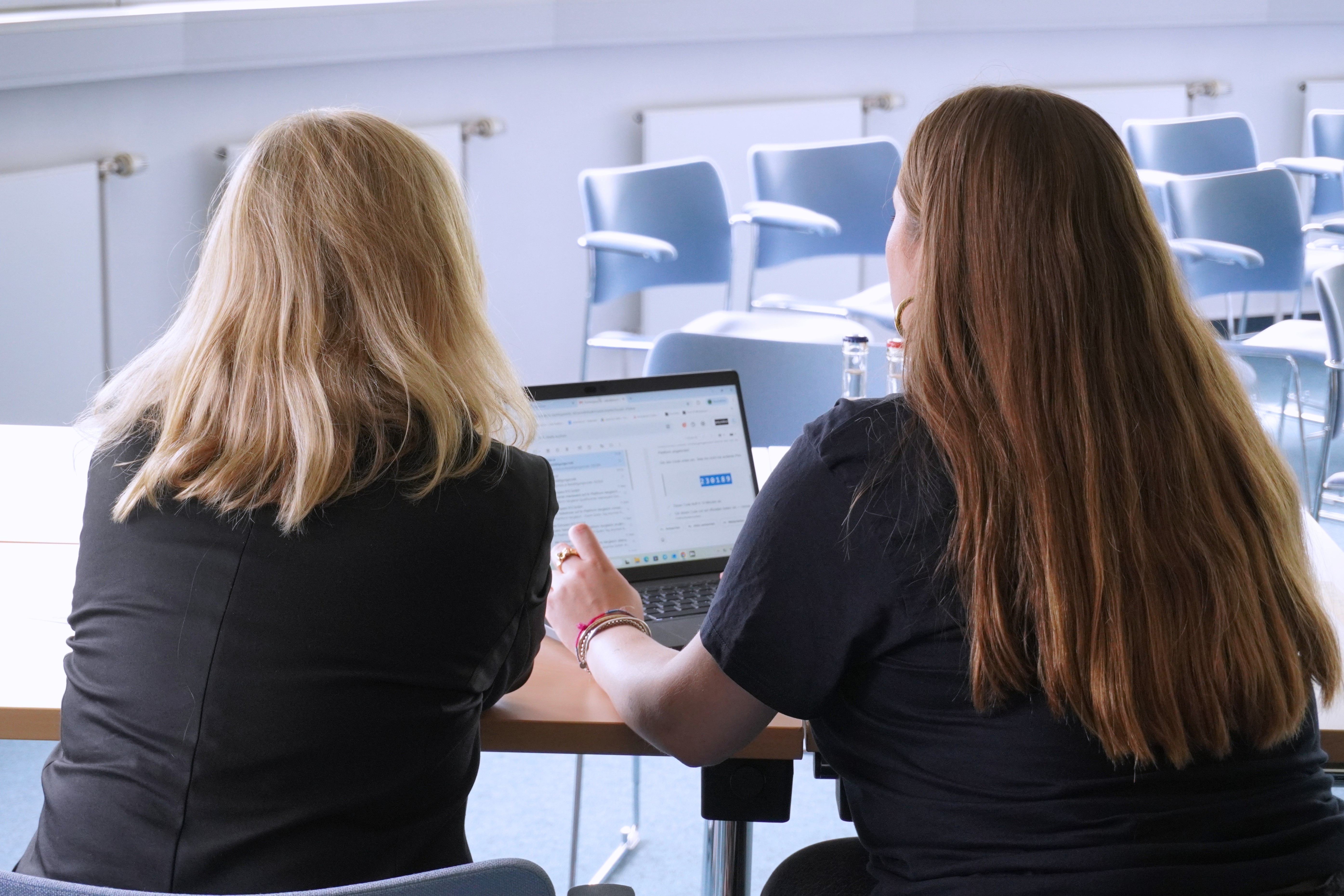 Zwei Frauen schauen von hinten gemeinsam in einen Laptop